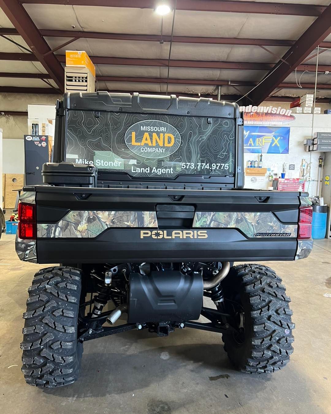 Black Polaris UTV seen from the rear in a warehouse, with muddy off-road tires and “LAND” on the rear window.
