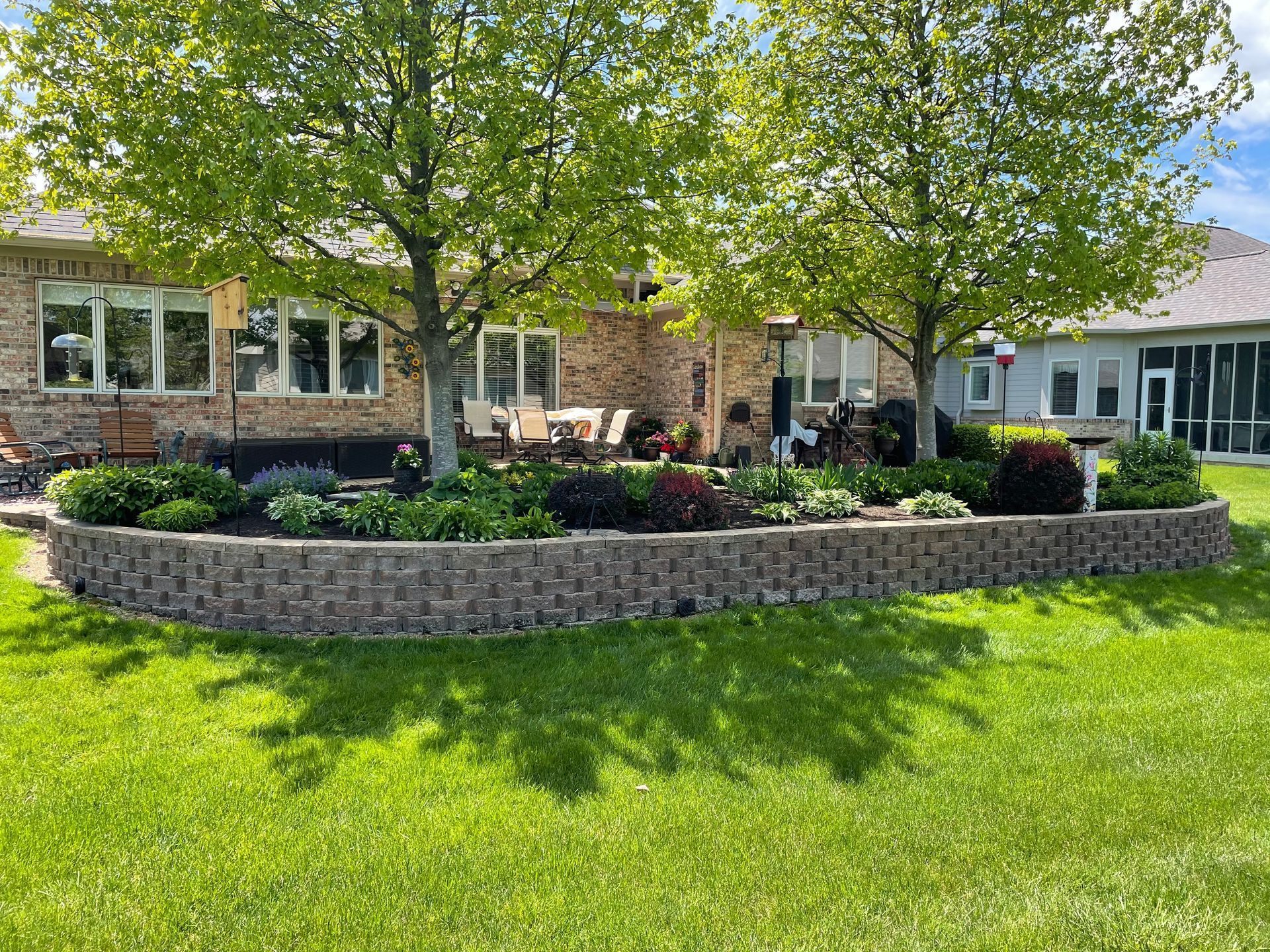 A large brick wall is in the middle of a lush green yard in front of a house.