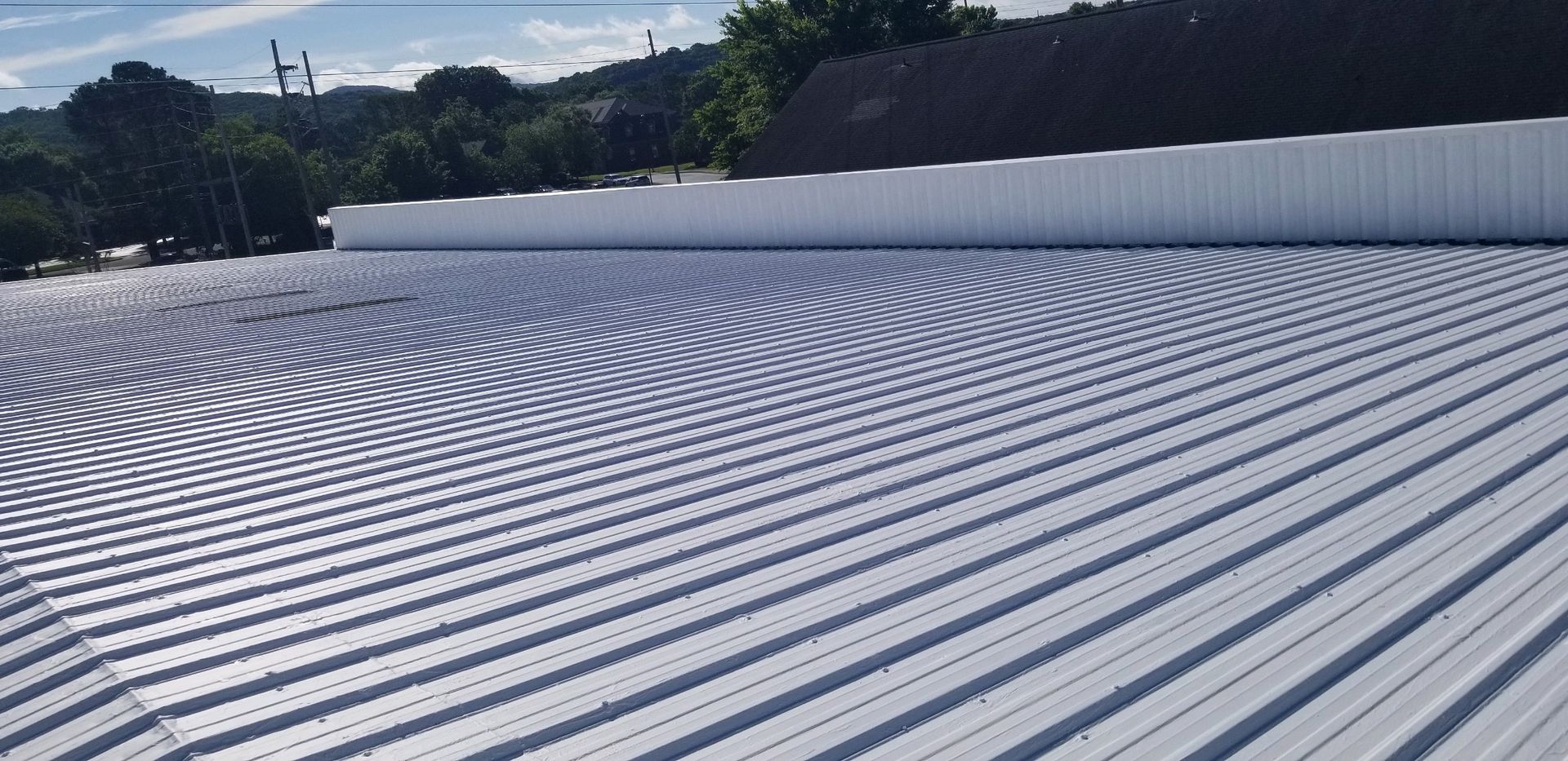 White corrugated metal roof with a white wall and a blue sky in the background.