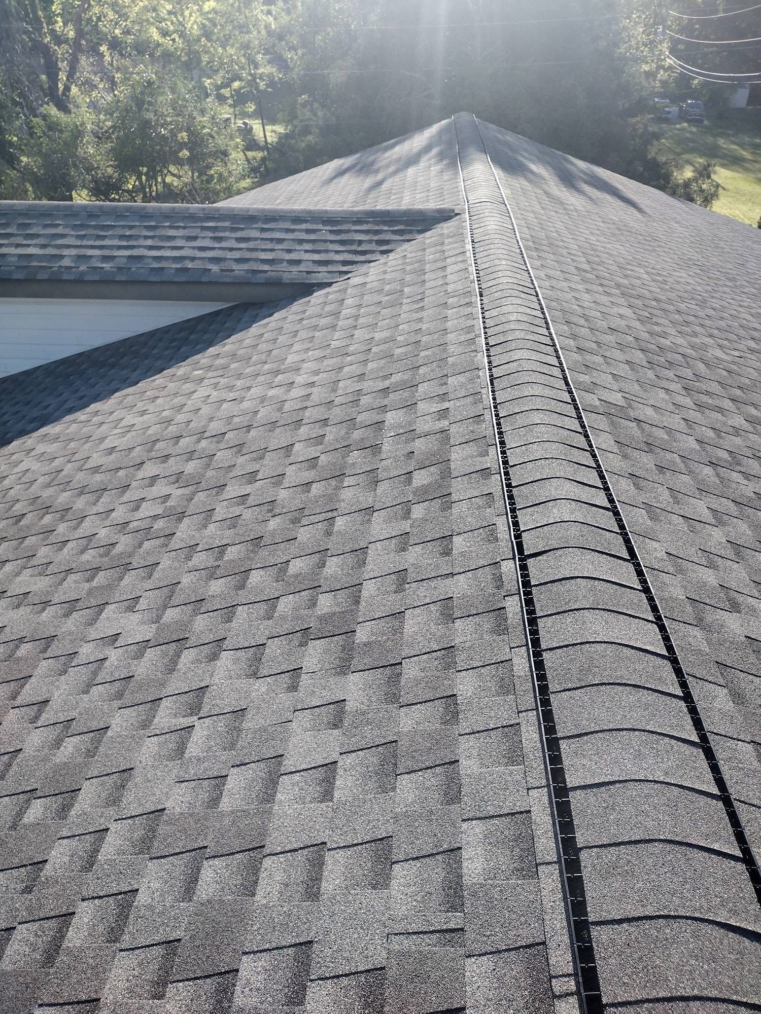 Dark gray shingled roof with a central ridge, viewed from above, sunlight visible.
