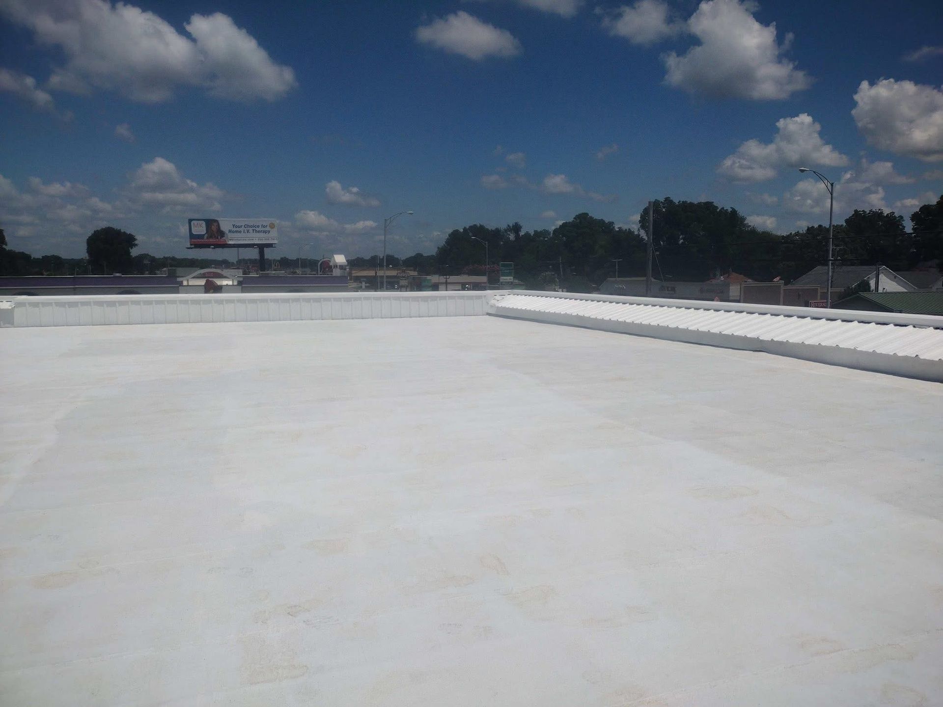 White commercial rooftop on a sunny day. Blue sky with clouds, trees in background.