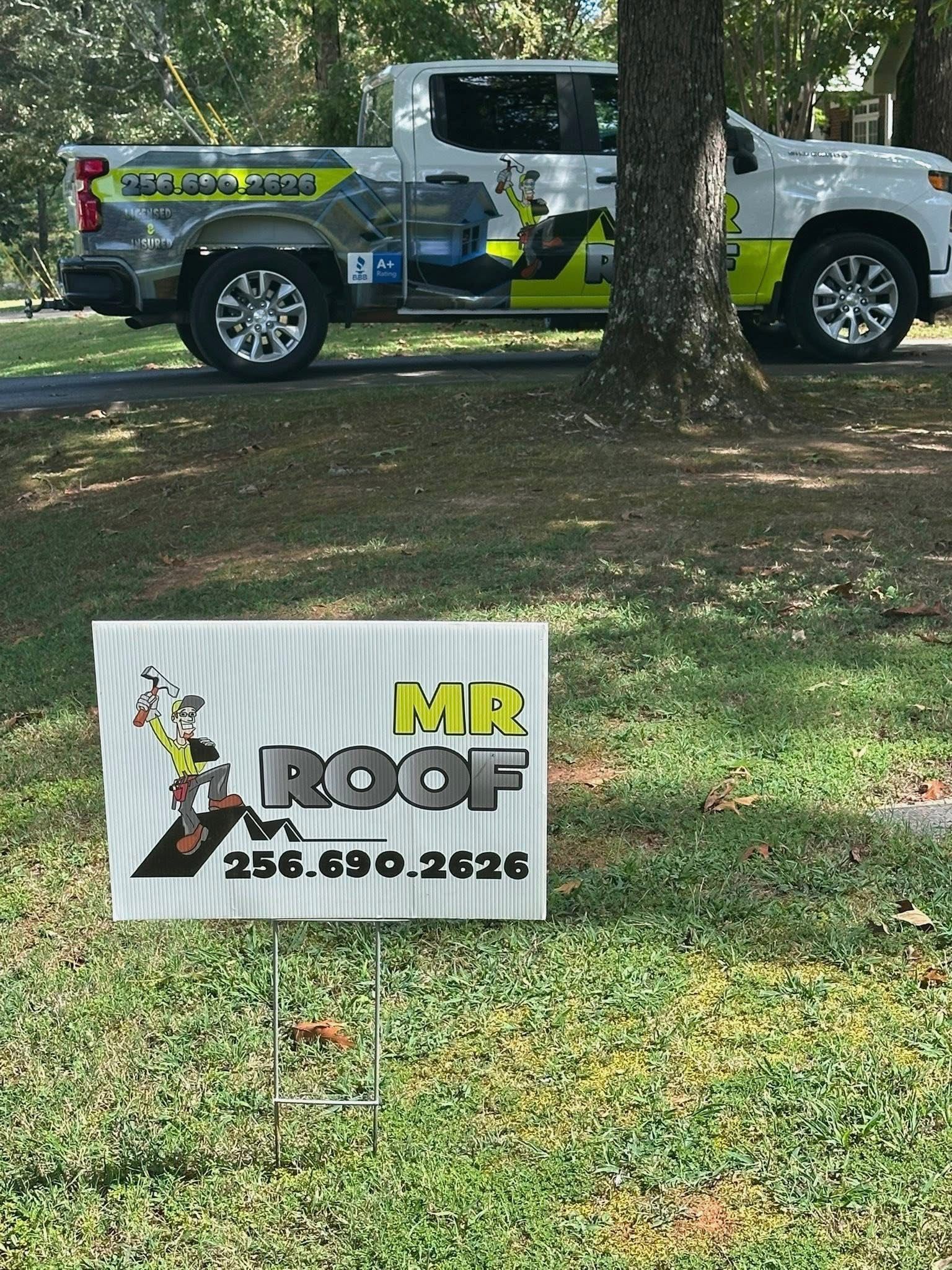 Sign for Mr. Roof with phone number, in front of their truck parked on grass.