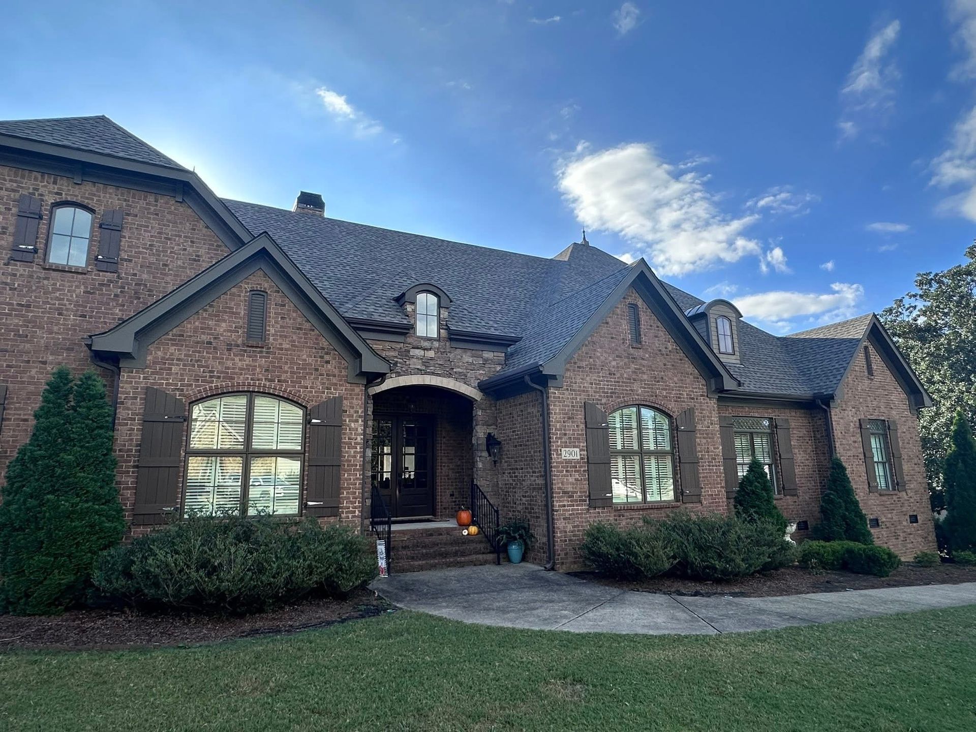 Brick house with brown shutters, dark roof, and blue sky.