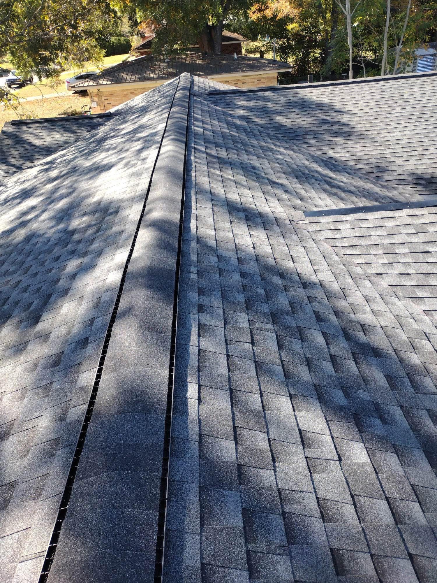 View of a dark gray shingled roof with a central ridge. The top is in daylight.