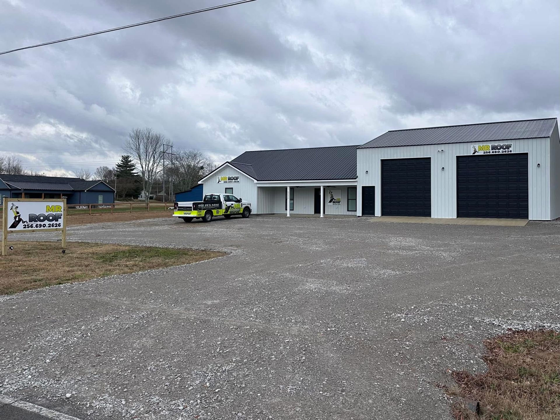 Gravel lot with commercial building, sign, and utility vehicle. White building with black doors under overcast sky.