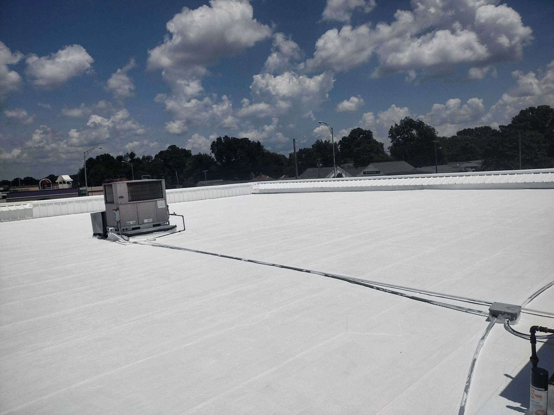 White roof with HVAC unit, electrical conduit, and cloudy blue sky.