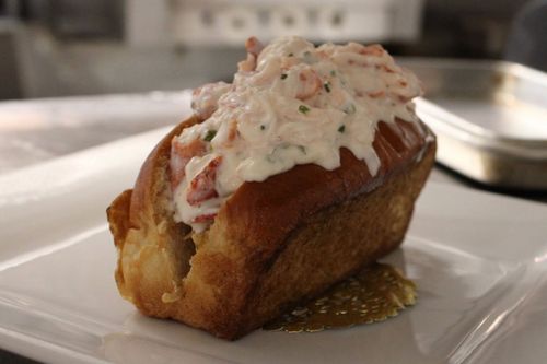 Crab-topped baked pastry on a white plate, with sauce and a blurred dining table in the background