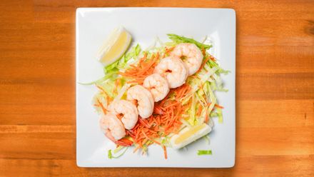 A shrimp cocktail platter featuring arranged cooked shrimp, a center bowl of red sauce, and a lemon wedge on a gold plate.