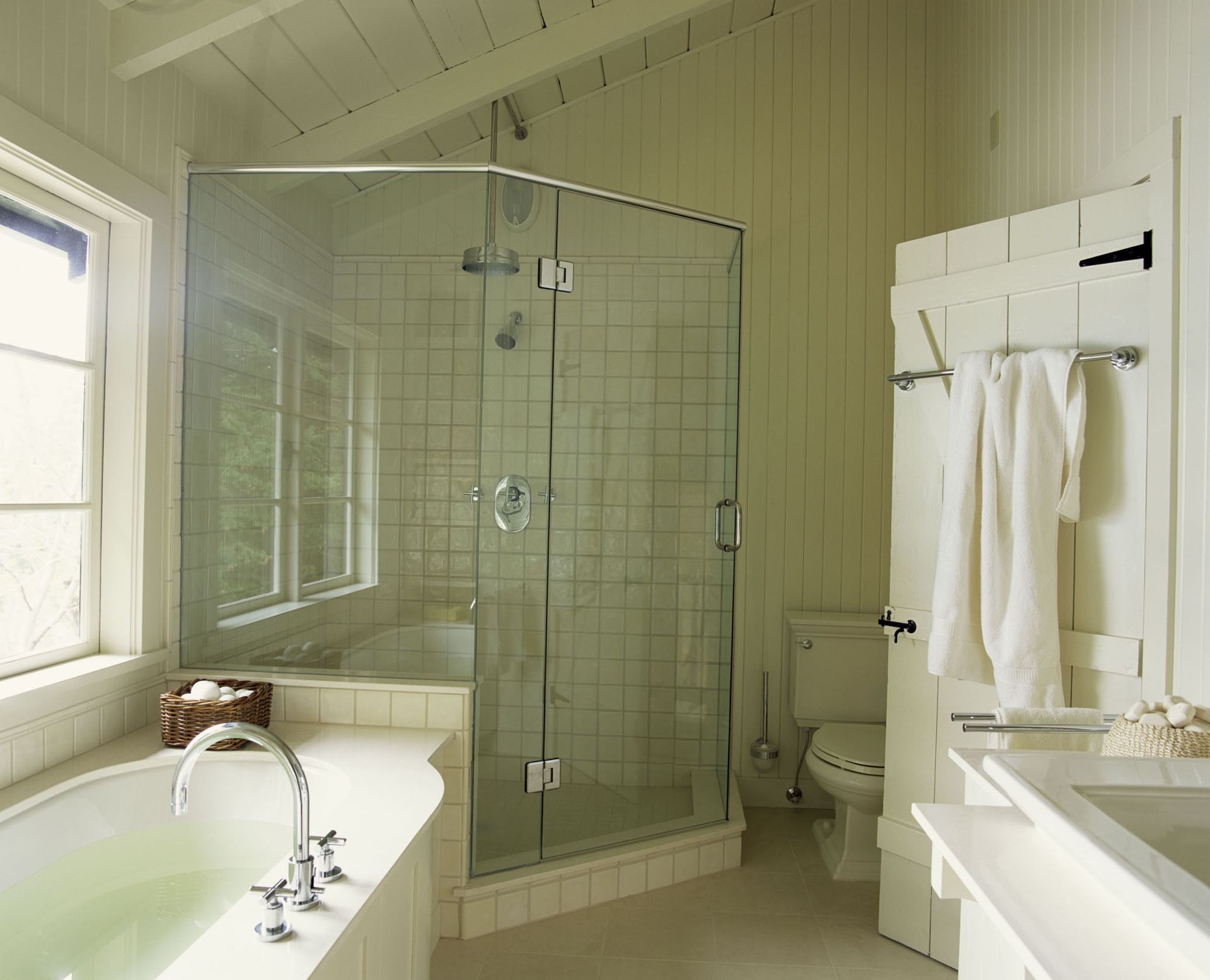 Bright bathroom with glass shower, bathtub by window, and white towels hanging on a rack.