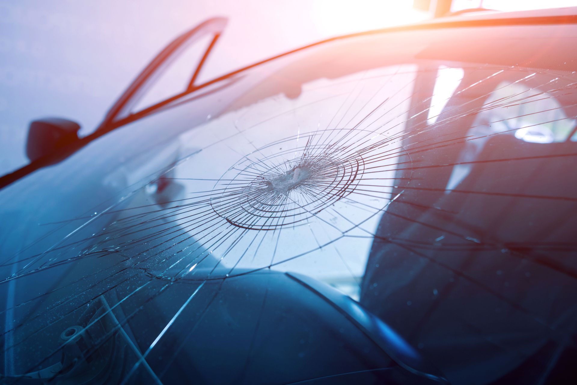 Shattered car windshield with cracked glass and blue reflections at sunset