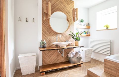 Bright modern bathroom with wood vanity, round mirror, white walls, and potted plants