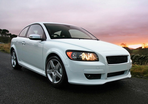 White sedan parked on a road at sunset with headlights on