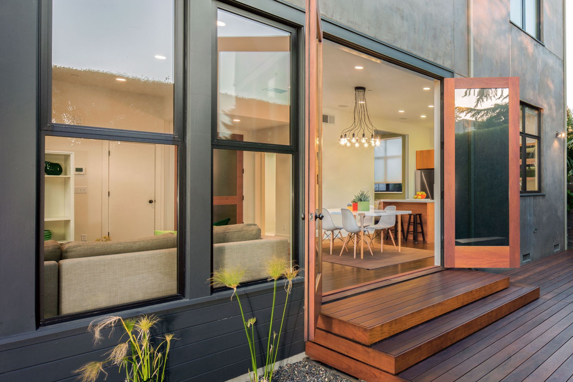 Modern home patio with open glass doors, wooden deck, and dining area visible inside