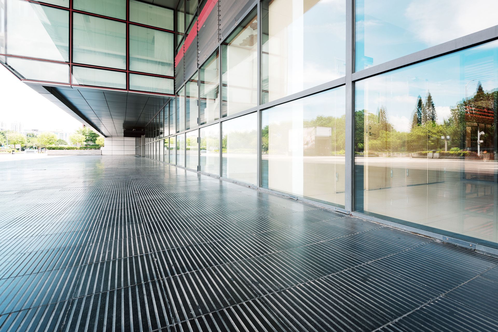Modern glass building walkway with patterned floor and reflections on large windows