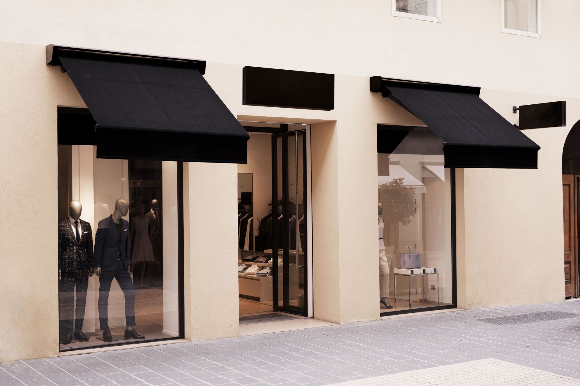 Storefront with three black awnings and large glass windows along a sidewalk.