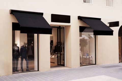 Storefront with three black awnings and large glass windows along a sidewalk.