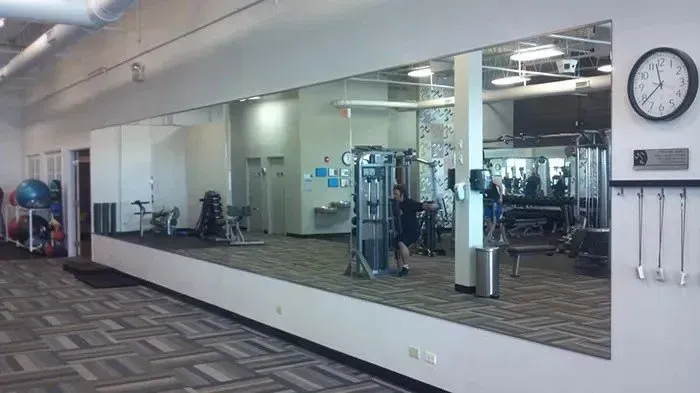 Empty gym interior with exercise machines, wall mirror, and a clock on the right wall