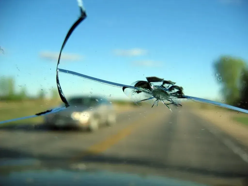 Cracked windshield on a blurred road with cars ahead and blue sky