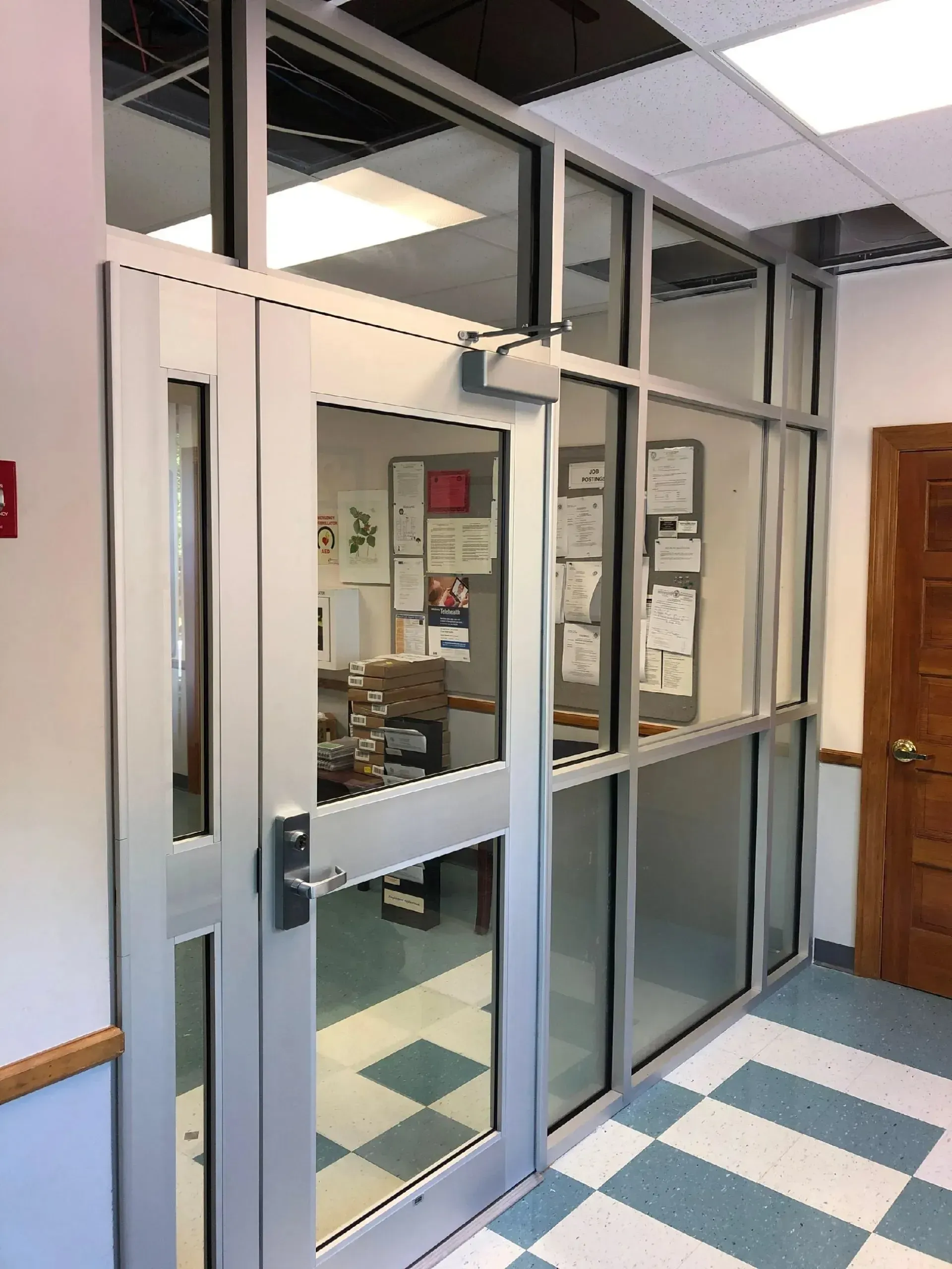Glass office entrance with double doors, blue-and-white tiled floor, and windows into a hallway office