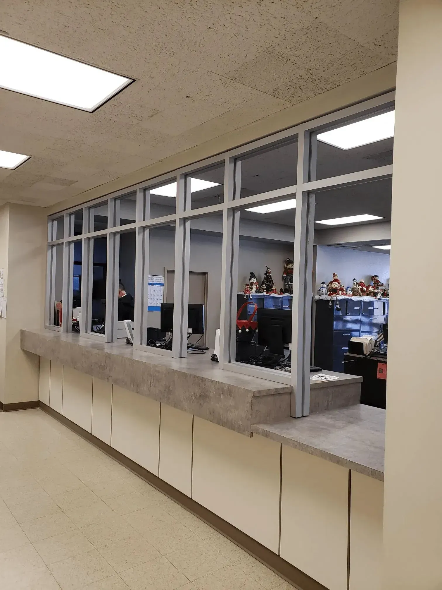 Hallway window to a computer lab with people working inside, fluorescent lights overhead