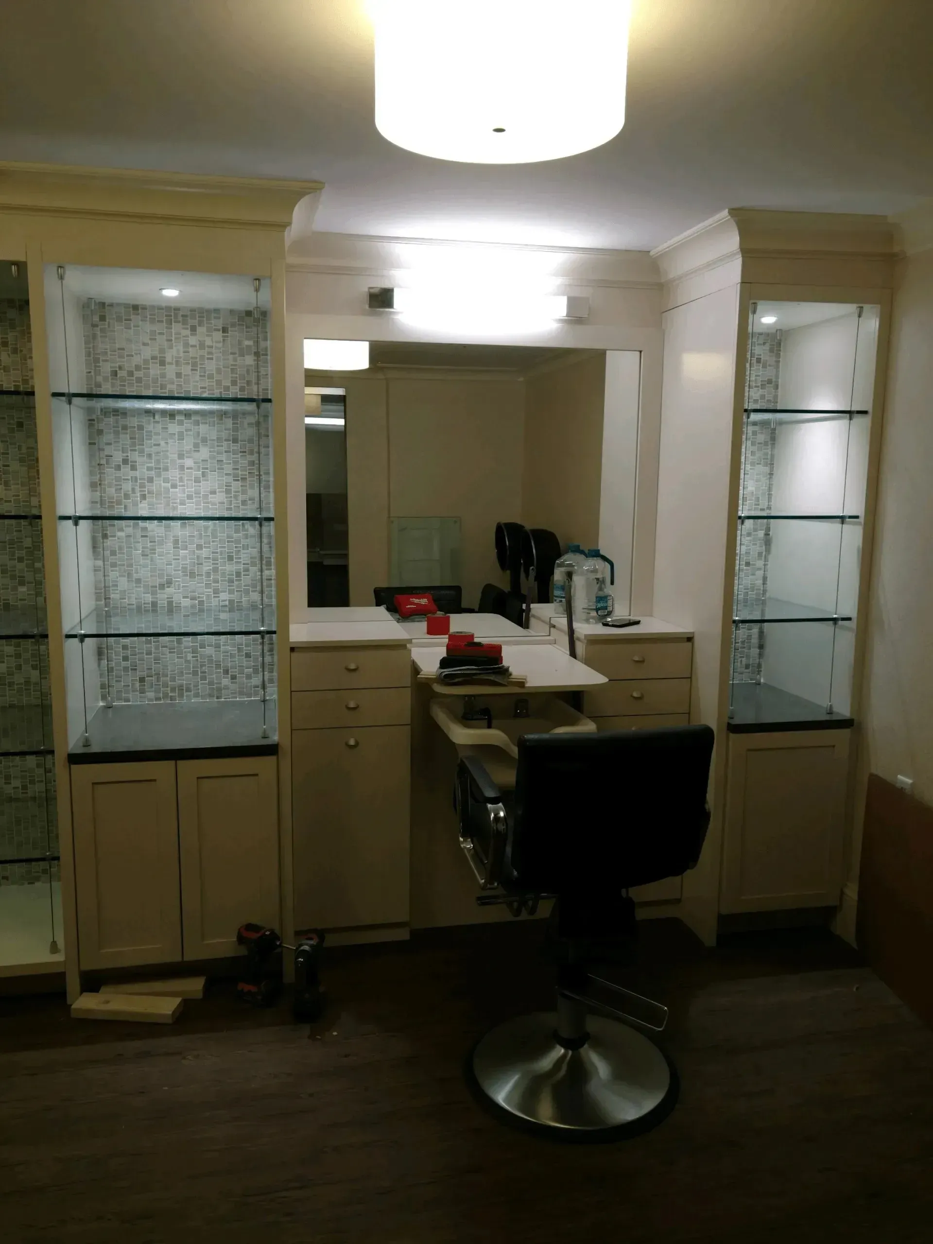 Salon vanity with mirrors, shelves, and a black styling chair under overhead lights
