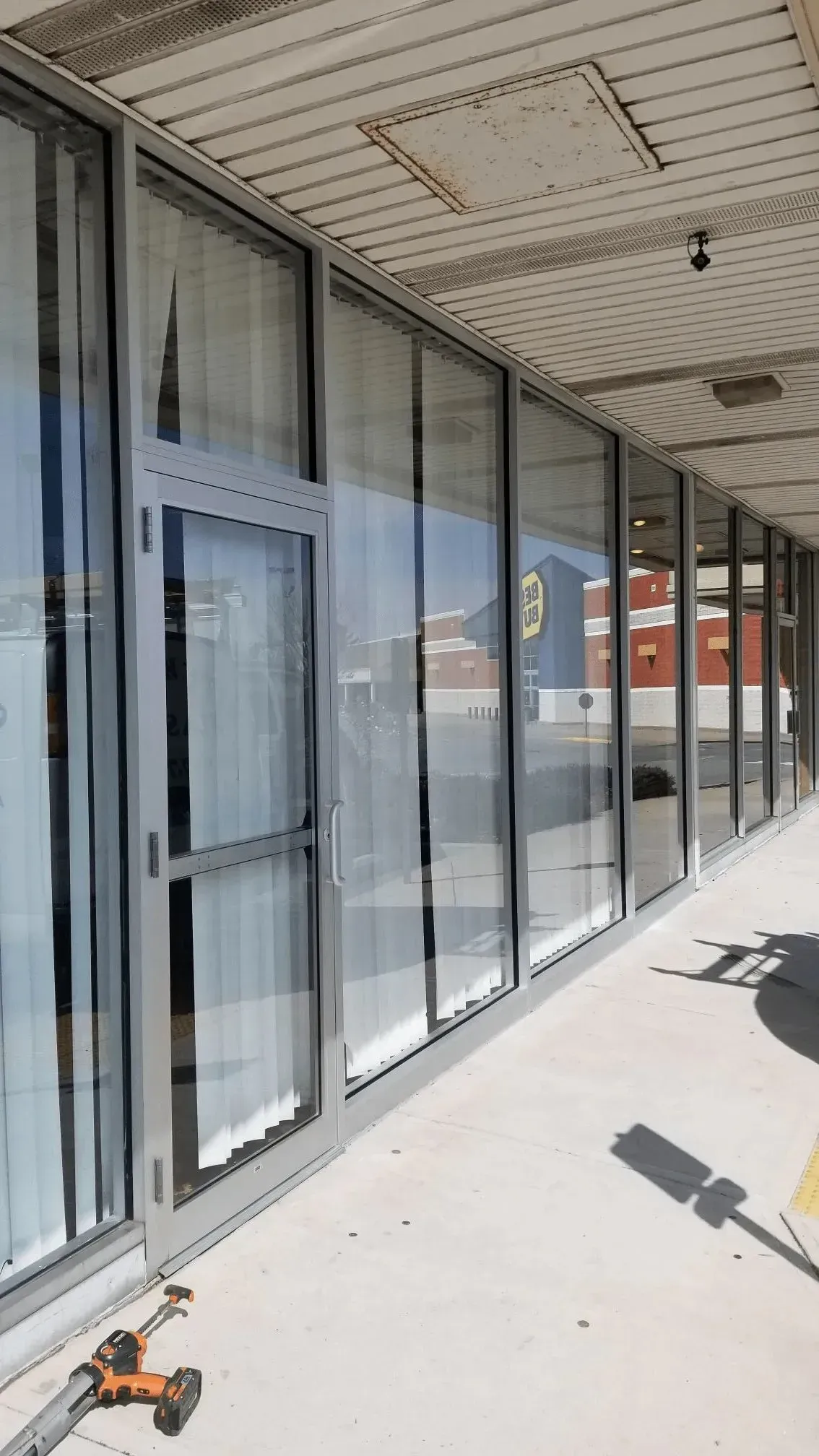 Storefront windows and doors along a covered walkway, with tools on the ground