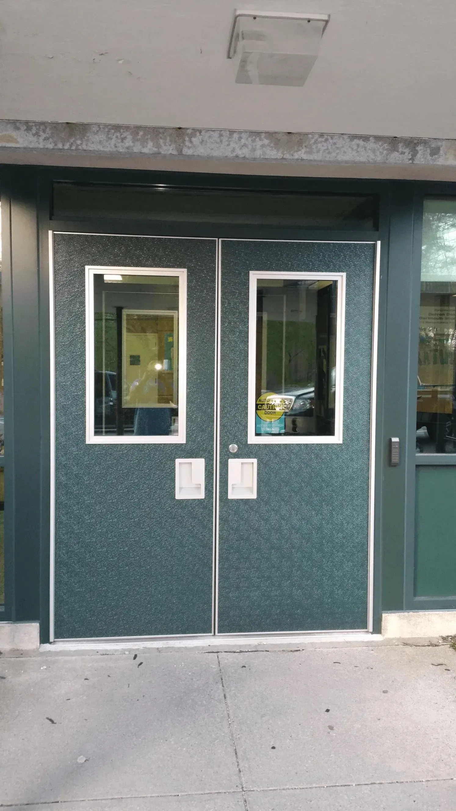 Green double doors with narrow windows at a building entrance