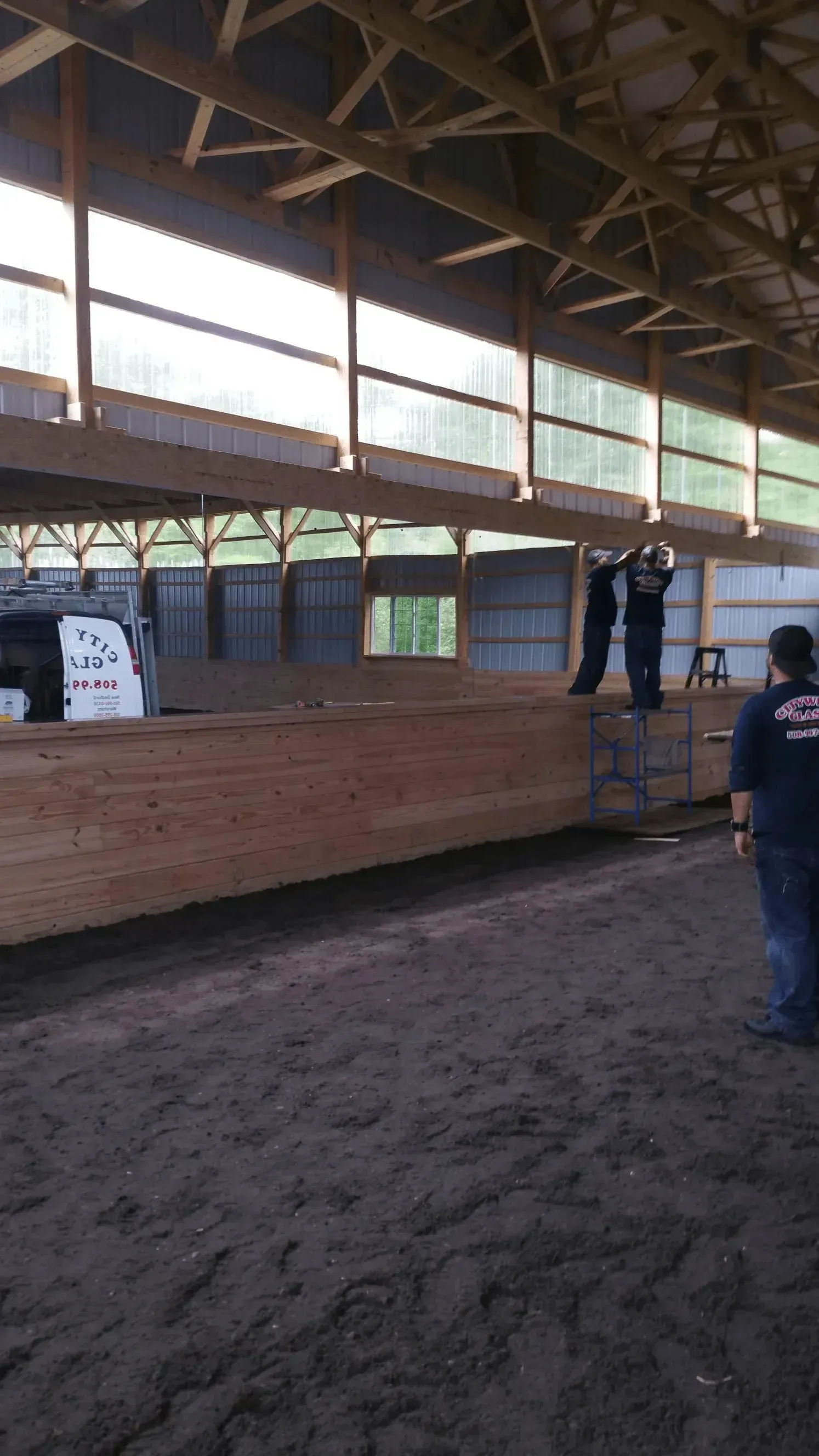 Indoor dirt arena with wooden grandstand seating and two people standing on a small blue step ladder.
