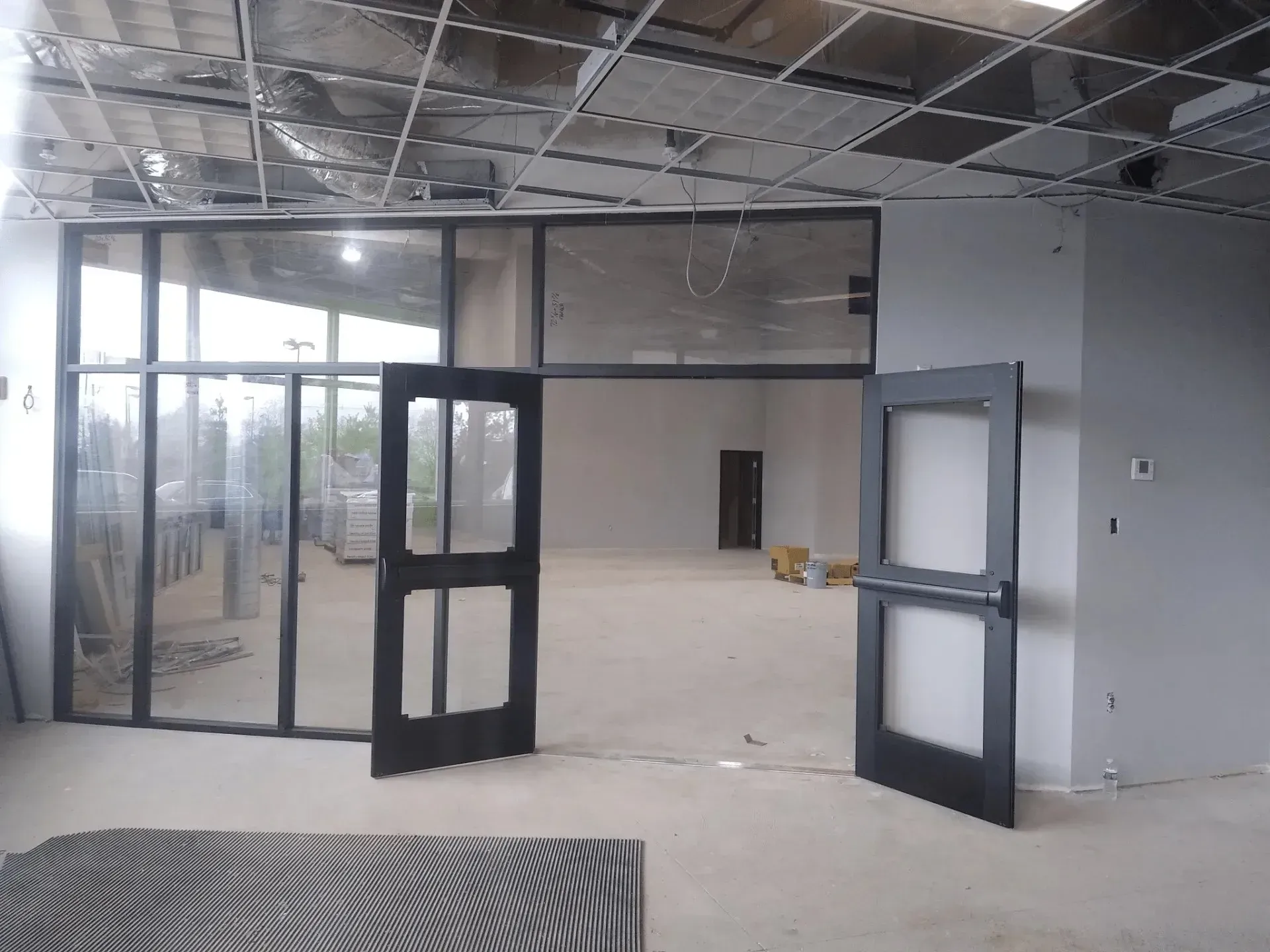 Empty office interior with glass partitions, open double doors, and unfinished ceiling and floor