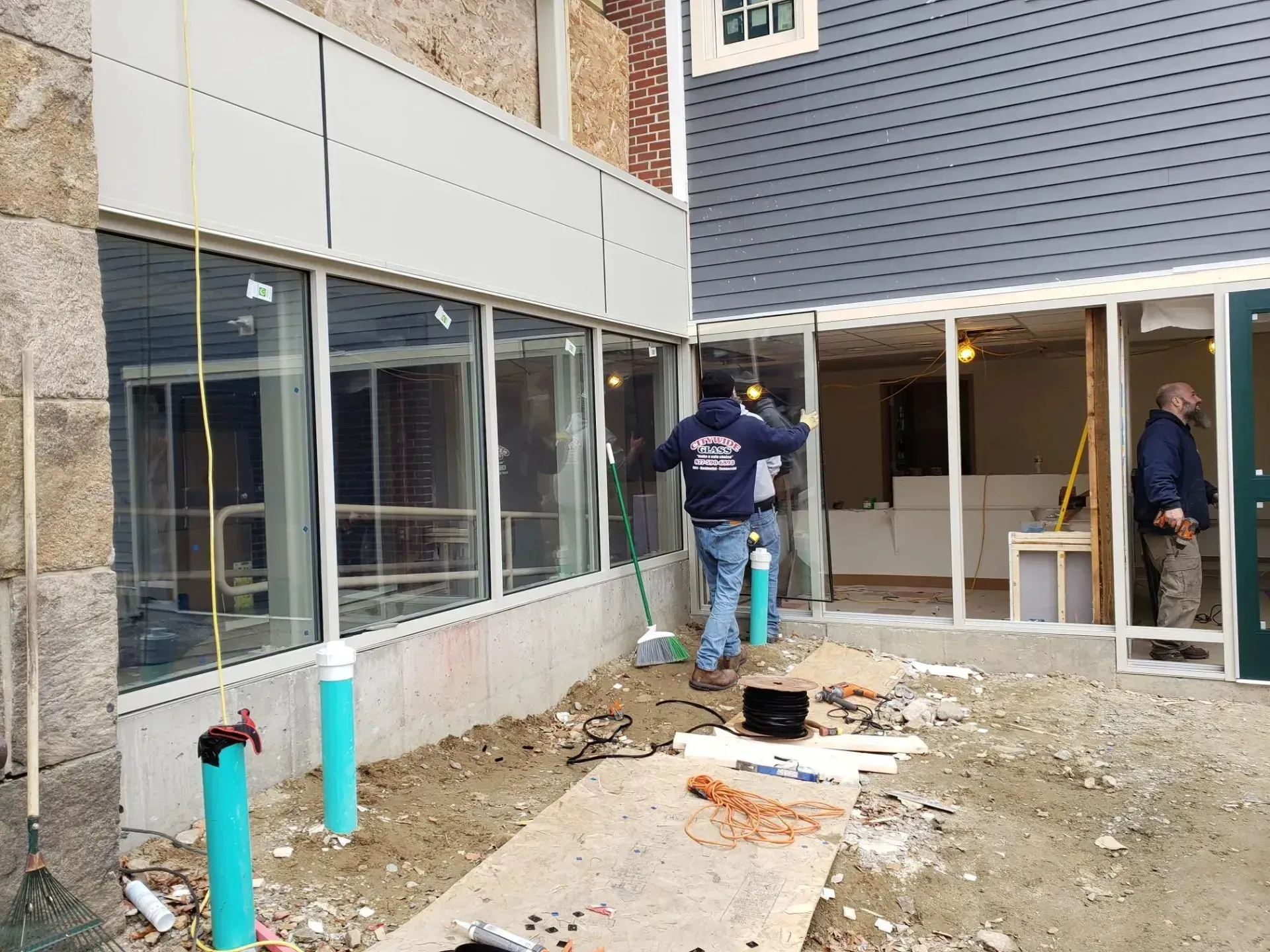 Construction workers repairing a narrow outdoor walkway beside a building, with debris and tools scattered around.