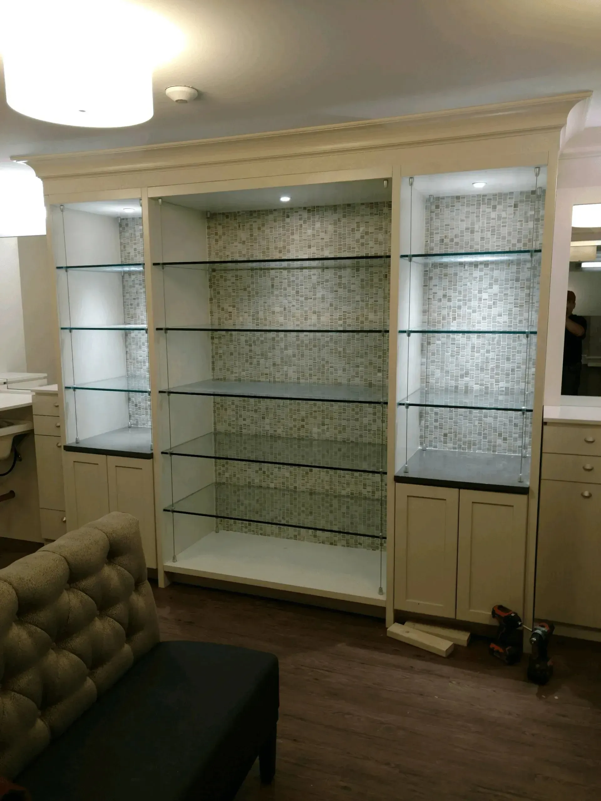 Empty glass display shelves in a living room, with a sofa edge and a ceiling light visible