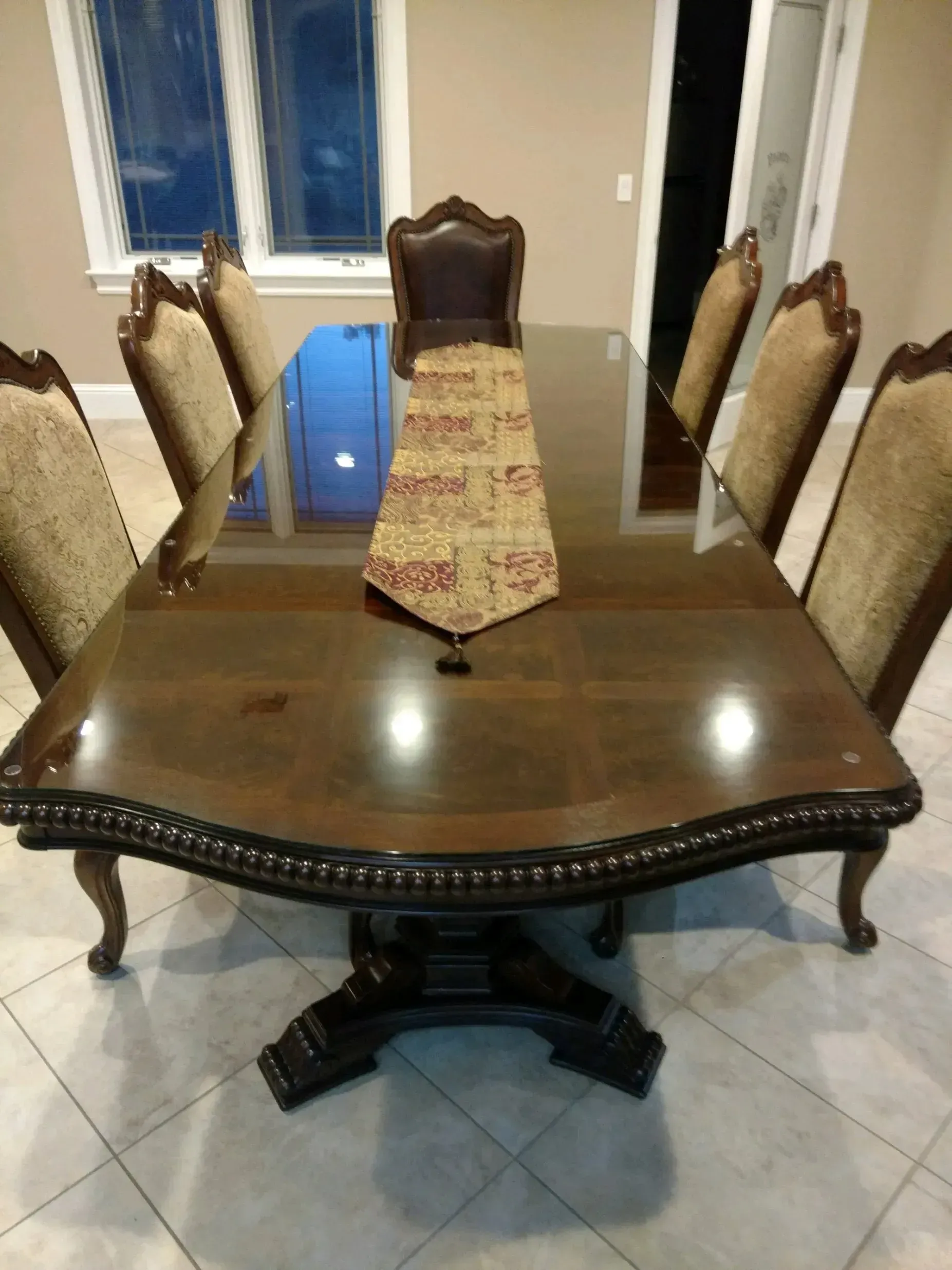 Wooden dining table with six carved chairs in a tiled room.