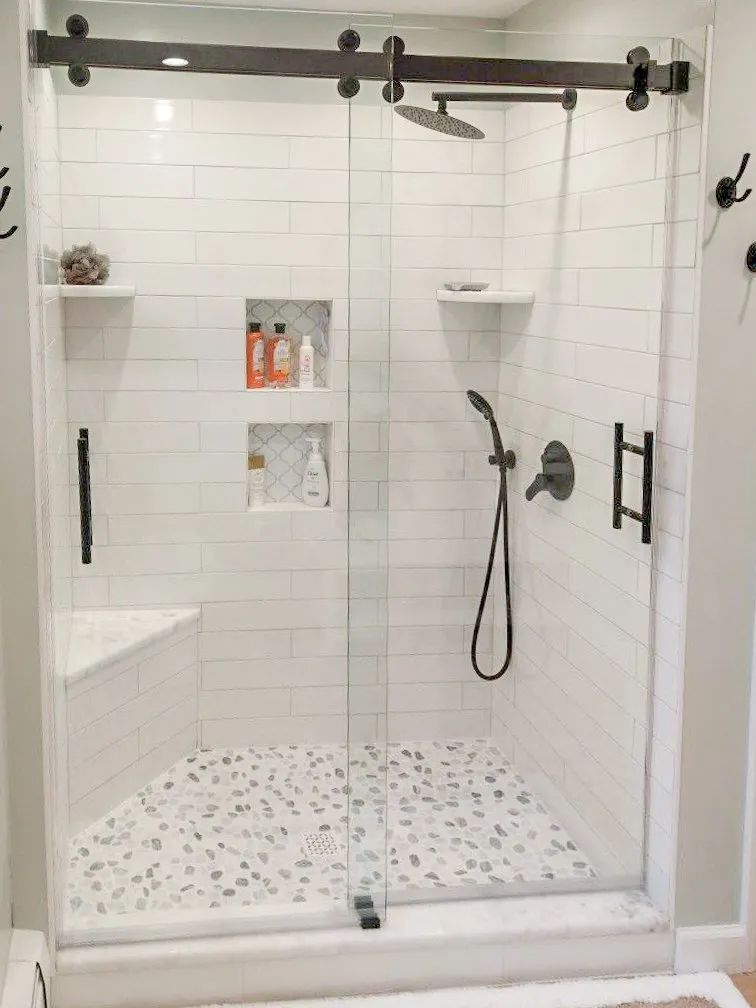 Modern white tiled walk-in shower with glass door, bench, niche shelves, and handheld showerhead