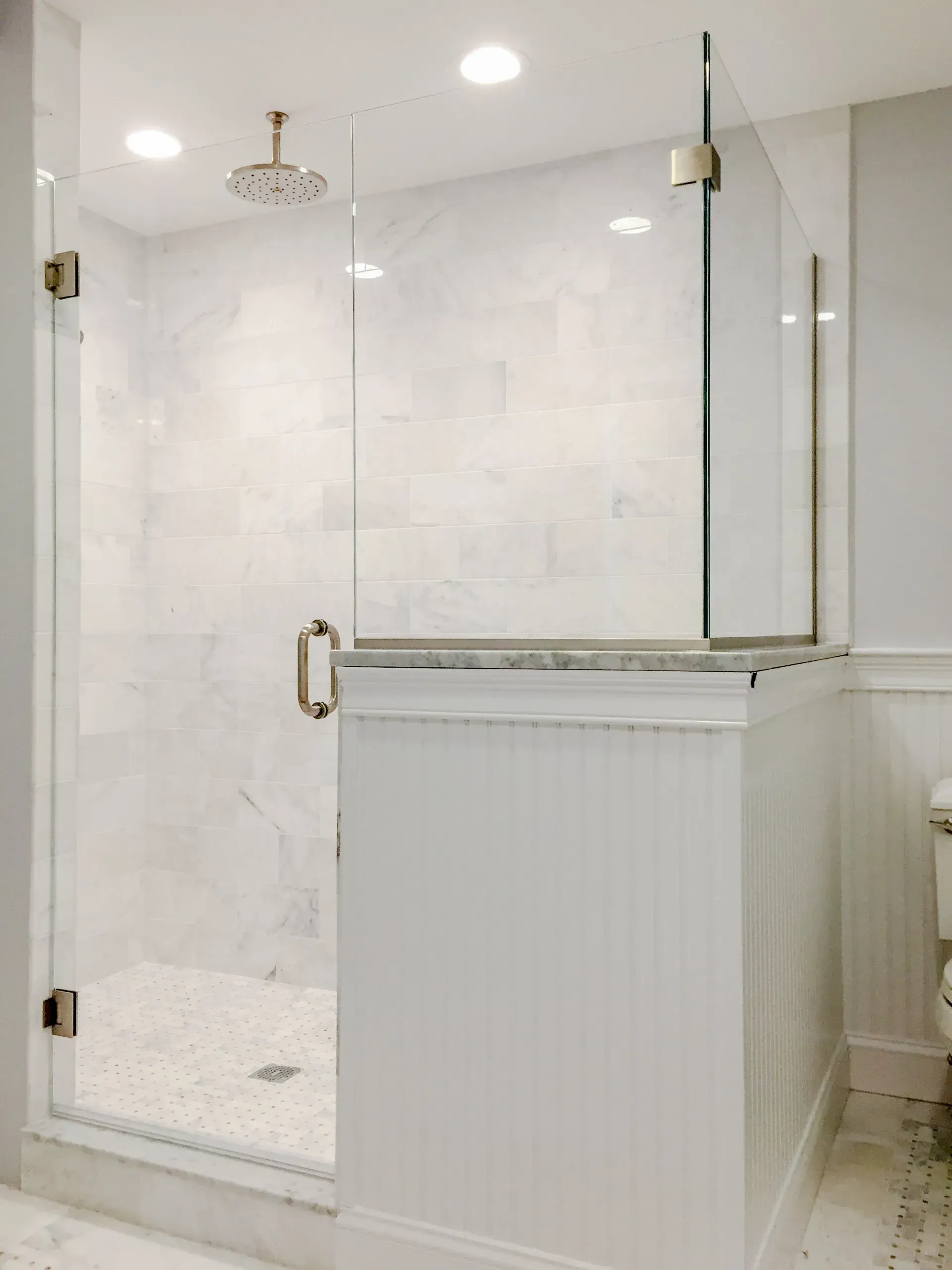 Glass-enclosed white marble shower with brass hardware and a white vanity cabinet.