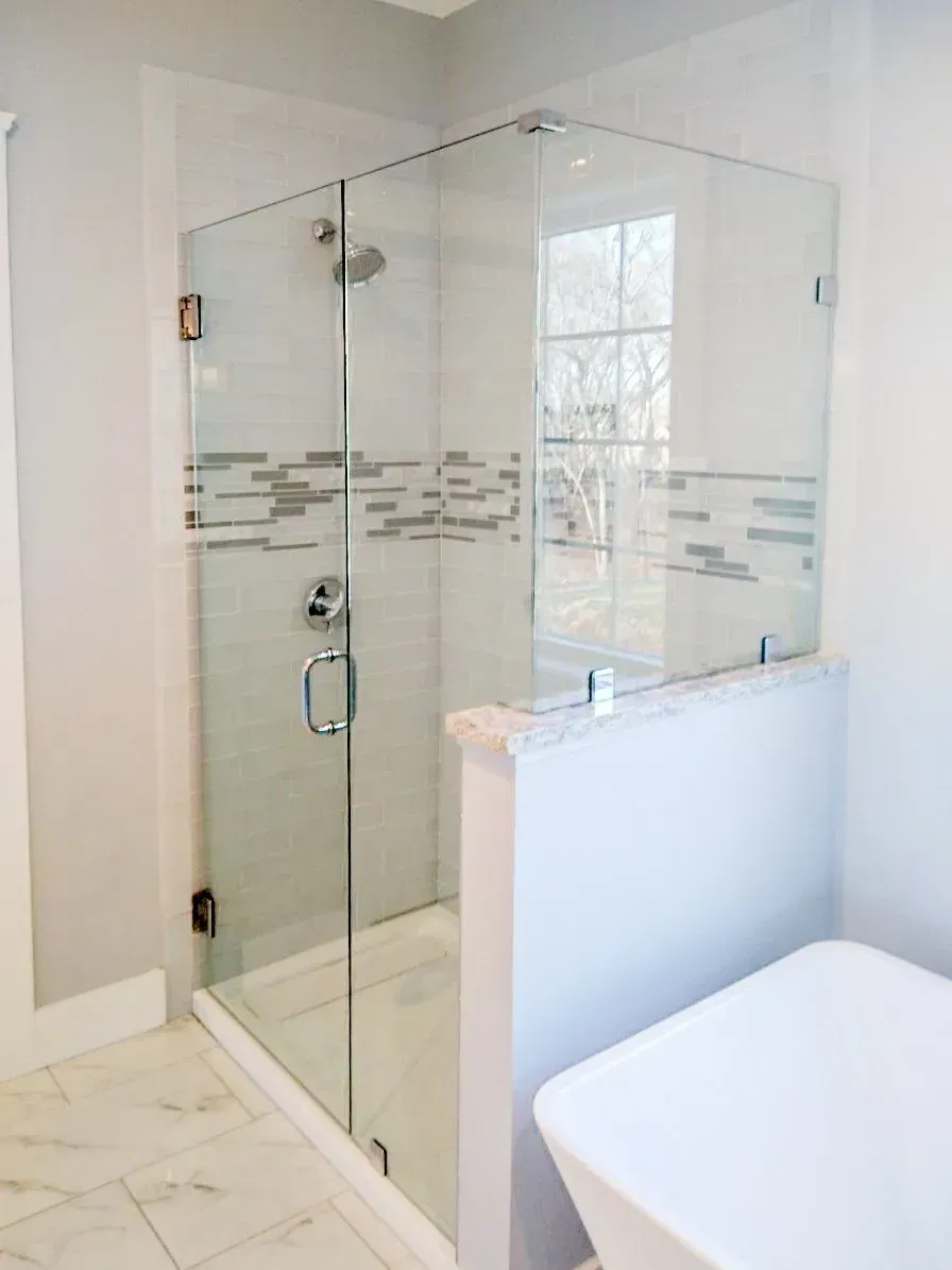 Modern glass shower enclosure in a bright white bathroom with marble tile and chrome fixtures