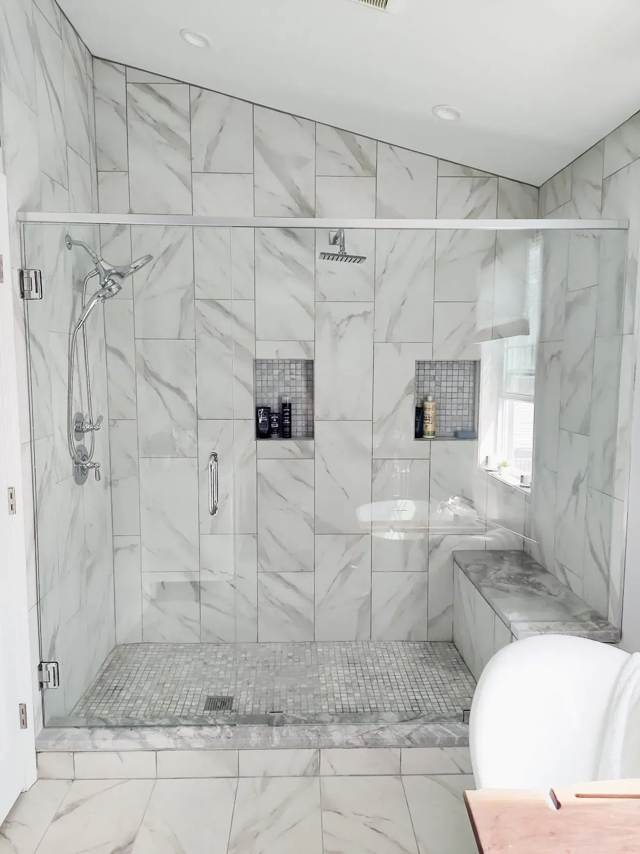 Modern marble-tiled bathroom with glass shower enclosure and bench seat