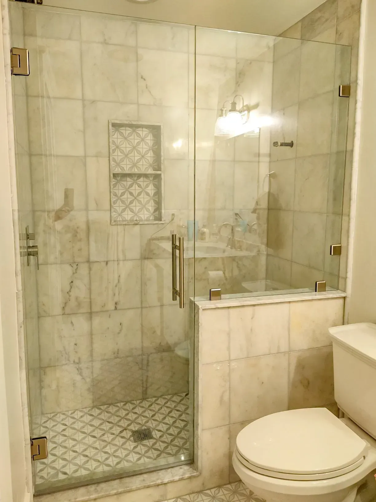 Glass-enclosed marble shower beside a toilet and vanity in a tiled bathroom