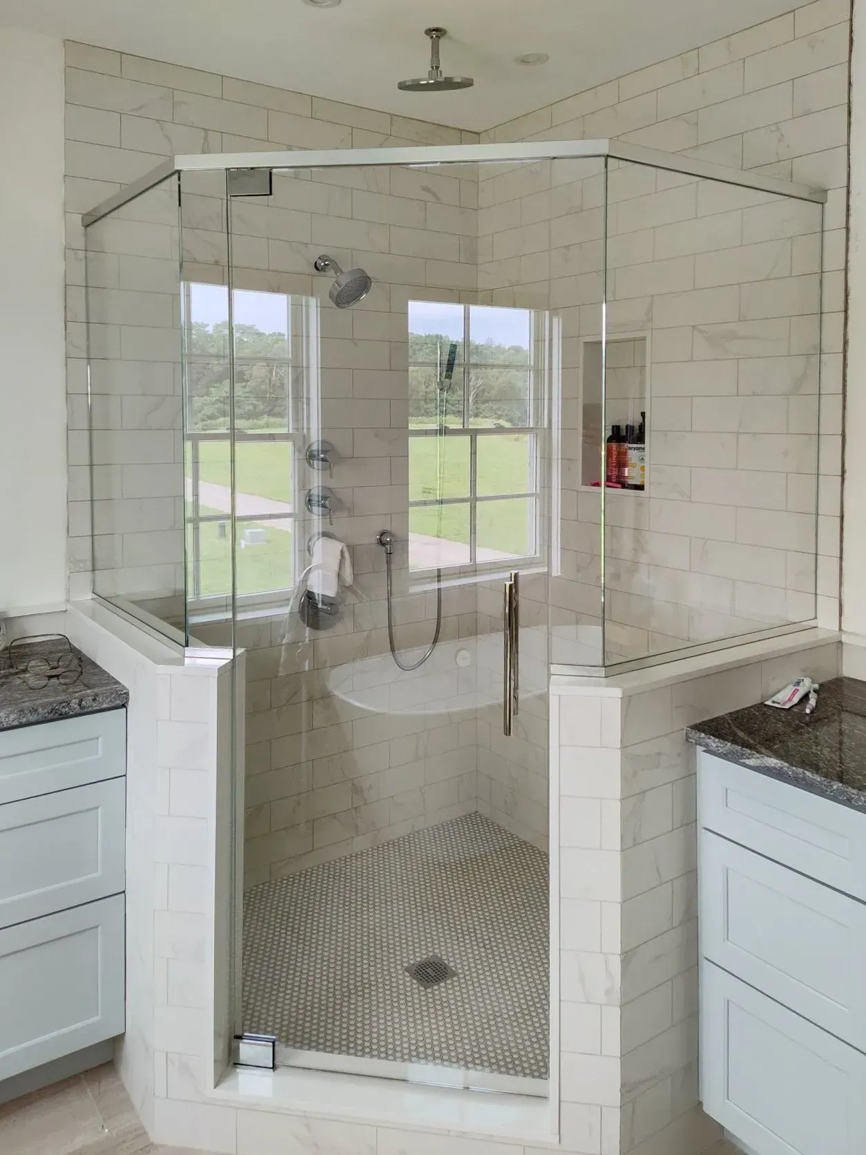 Walk-in glass shower with white subway tile and hex floor in a bright bathroom
