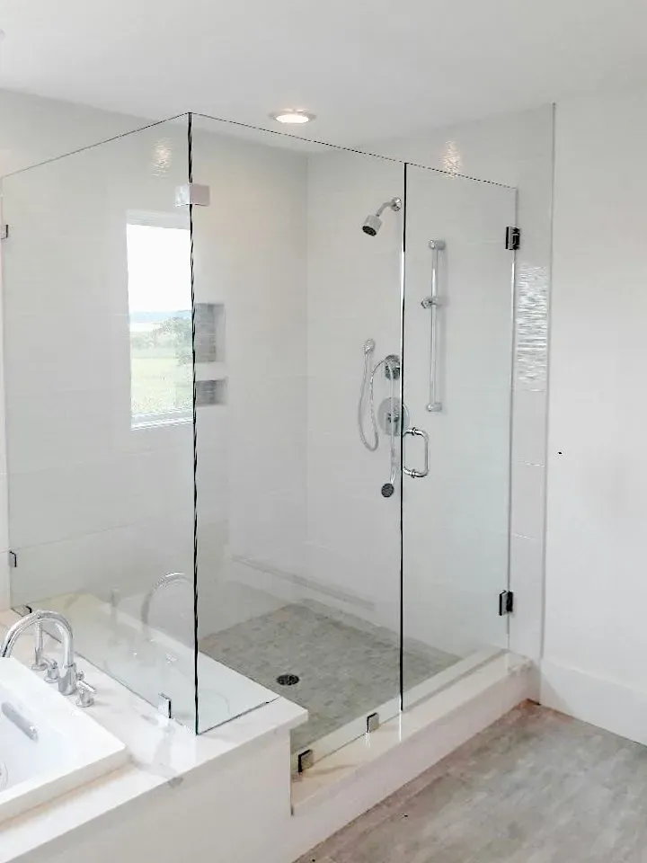 Glass walk-in shower with white tile walls, chrome fixtures, and a built-in bench in a bright bathroom
