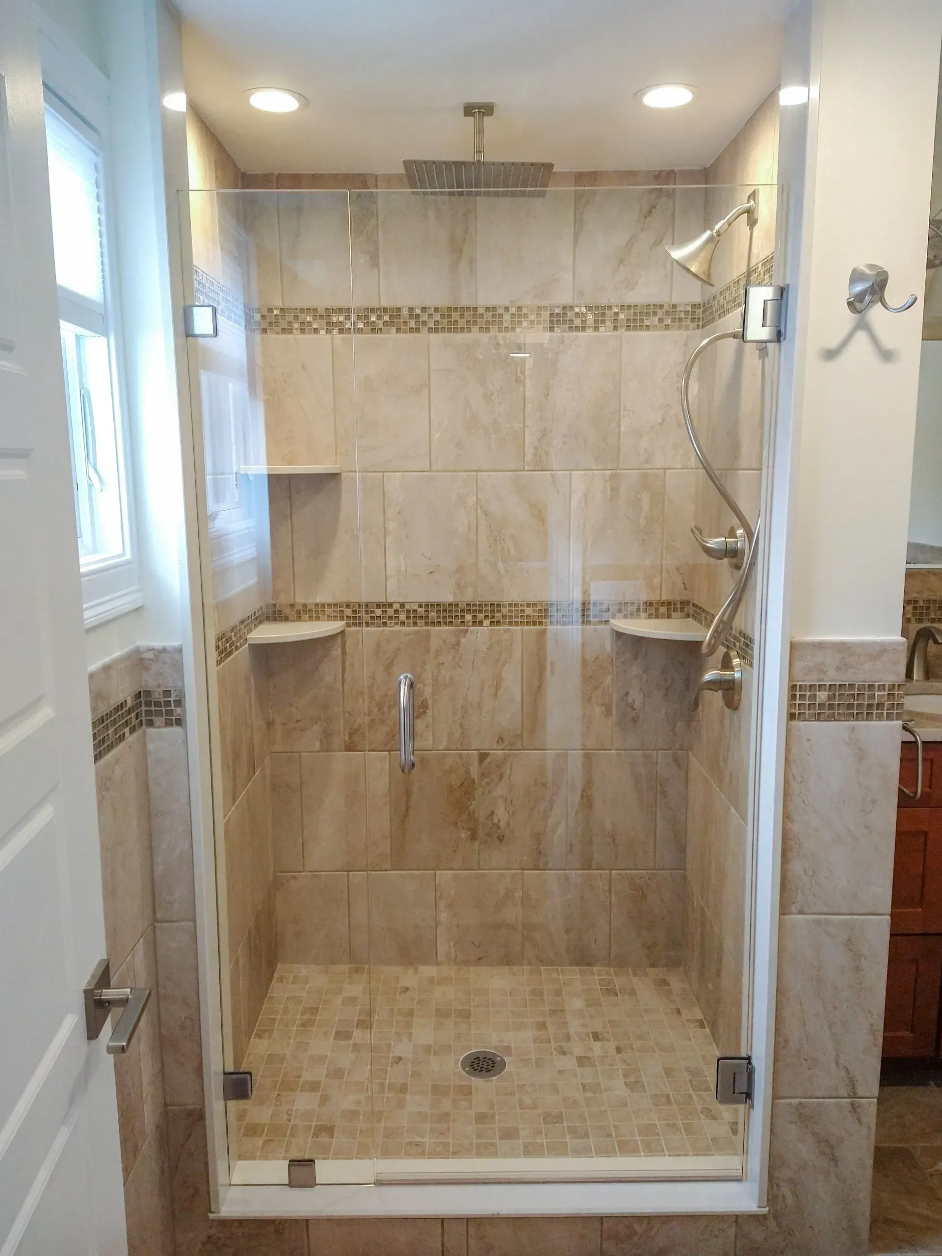 Glass walk-in shower with beige tile walls, built-in shelf, and chrome fixtures