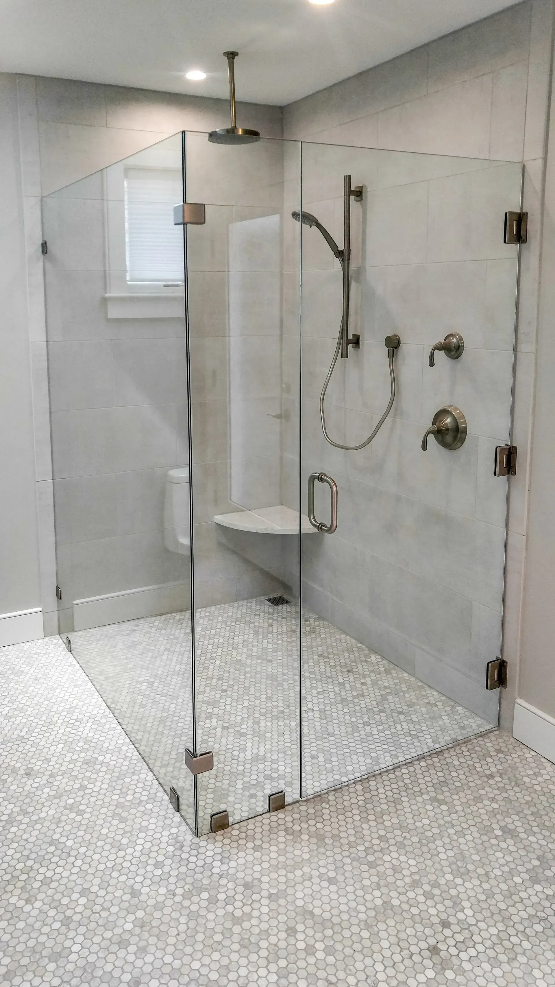 Modern glass walk-in shower with a handheld showerhead and pebble-textured floor in a bright bathroom