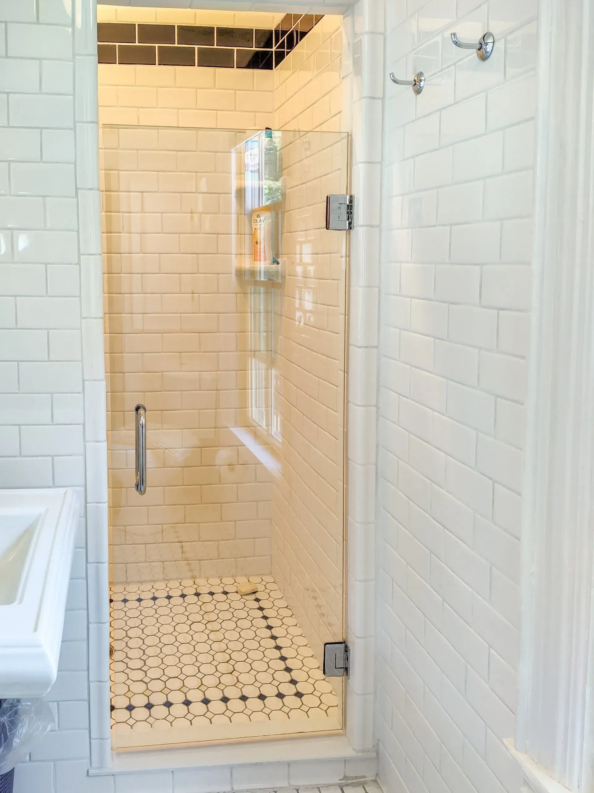 Glass shower stall with white subway tile and black-and-white mosaic floor in a bright bathroom