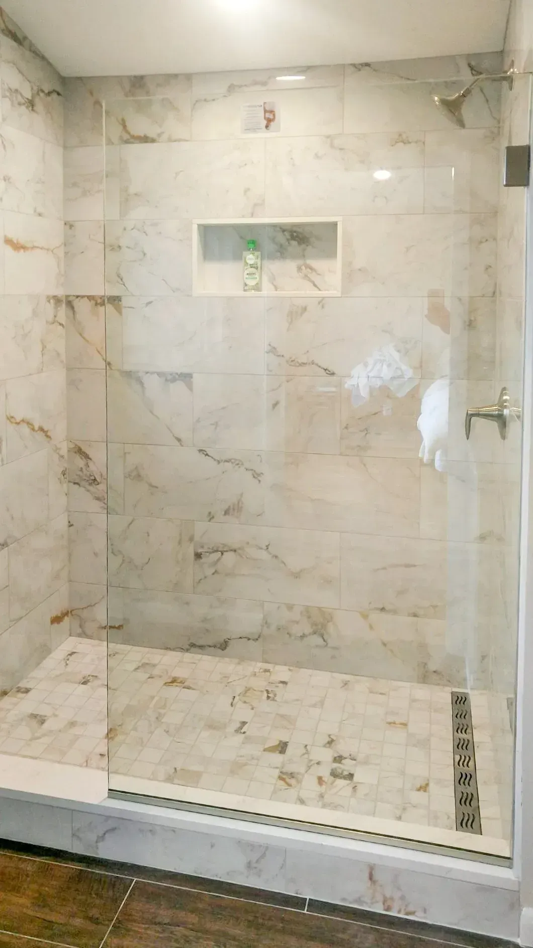 Empty beige tiled shower with built-in shelf and glass door