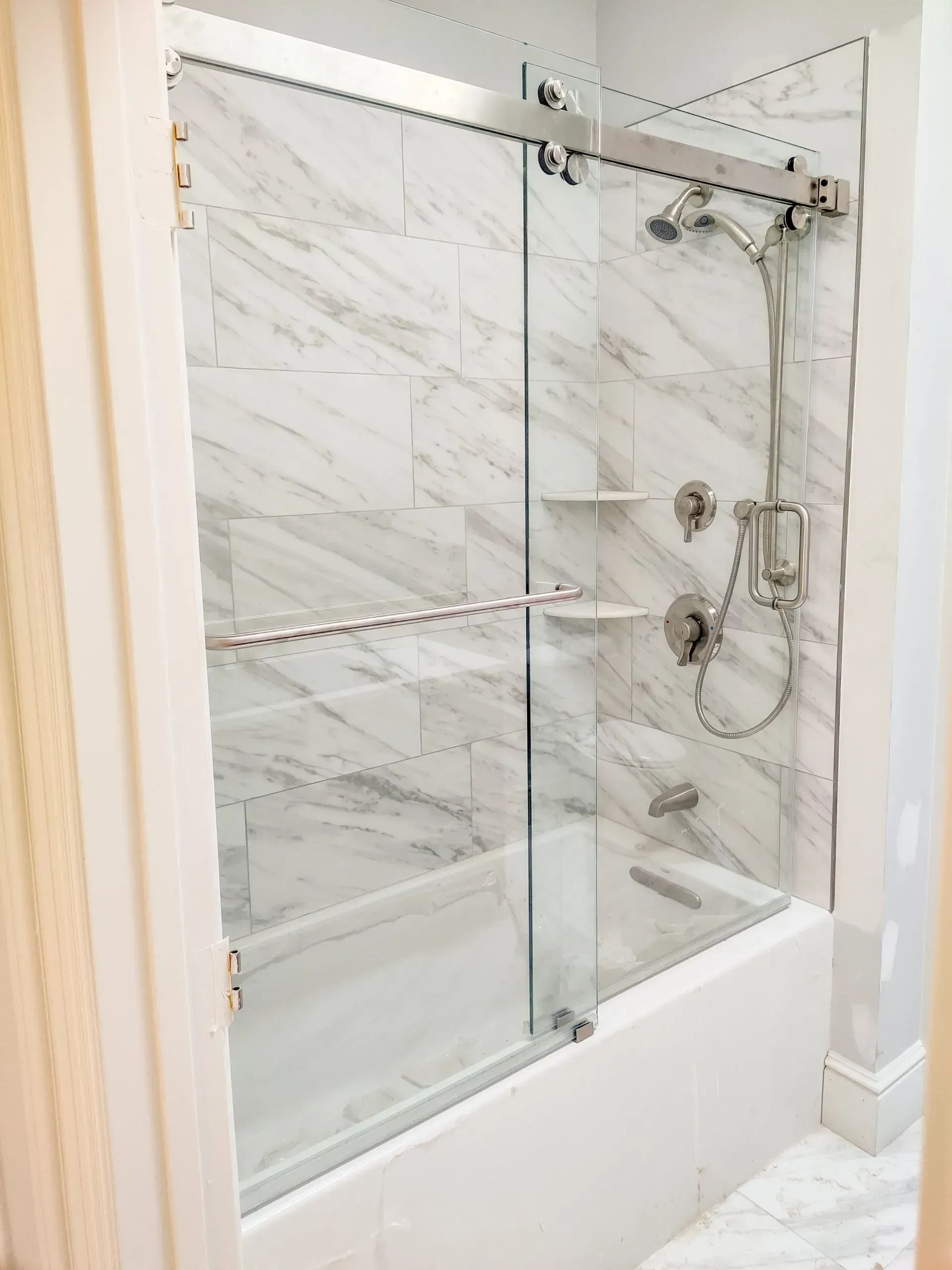 Glass walk-in shower with marble-pattern tile and chrome shower fixtures