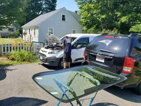 Severe car crash with damaged vehicles in a driveway, one hood crumpled and a person standing beside an open door