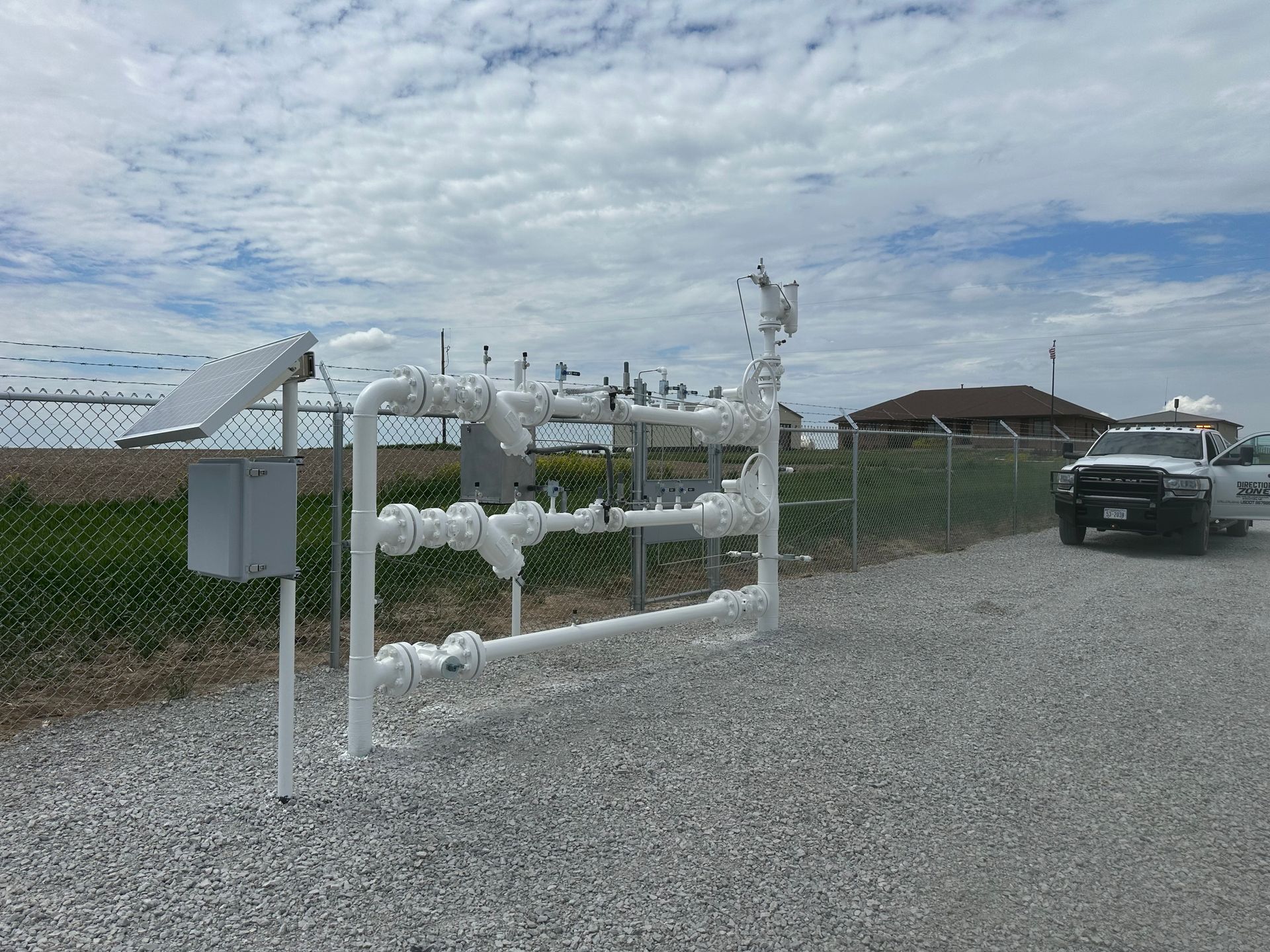 A white truck is parked in front of a fence and pipes.