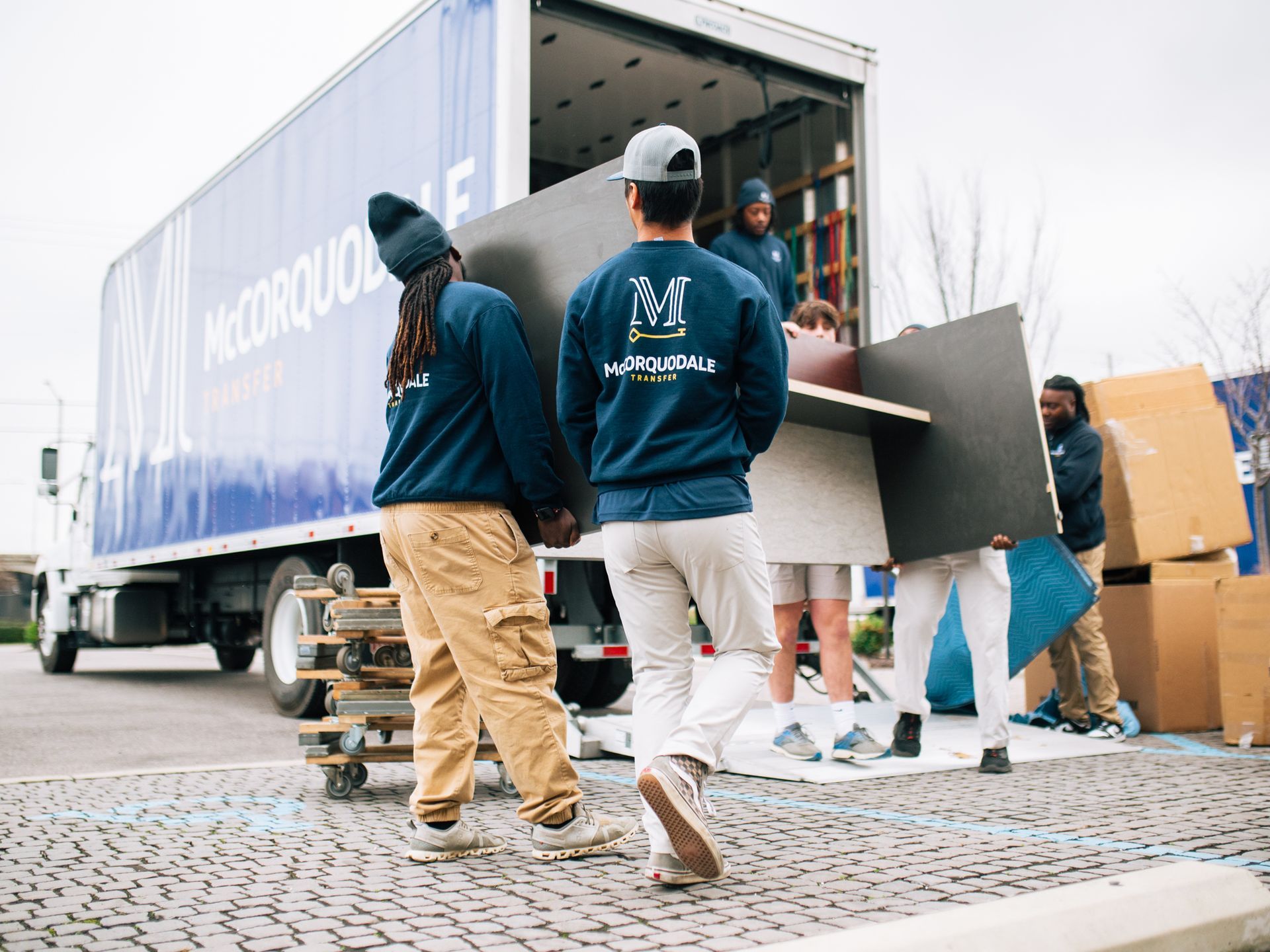 Movers unloading furniture from a truck onto a paved area, wearing matching uniforms.
