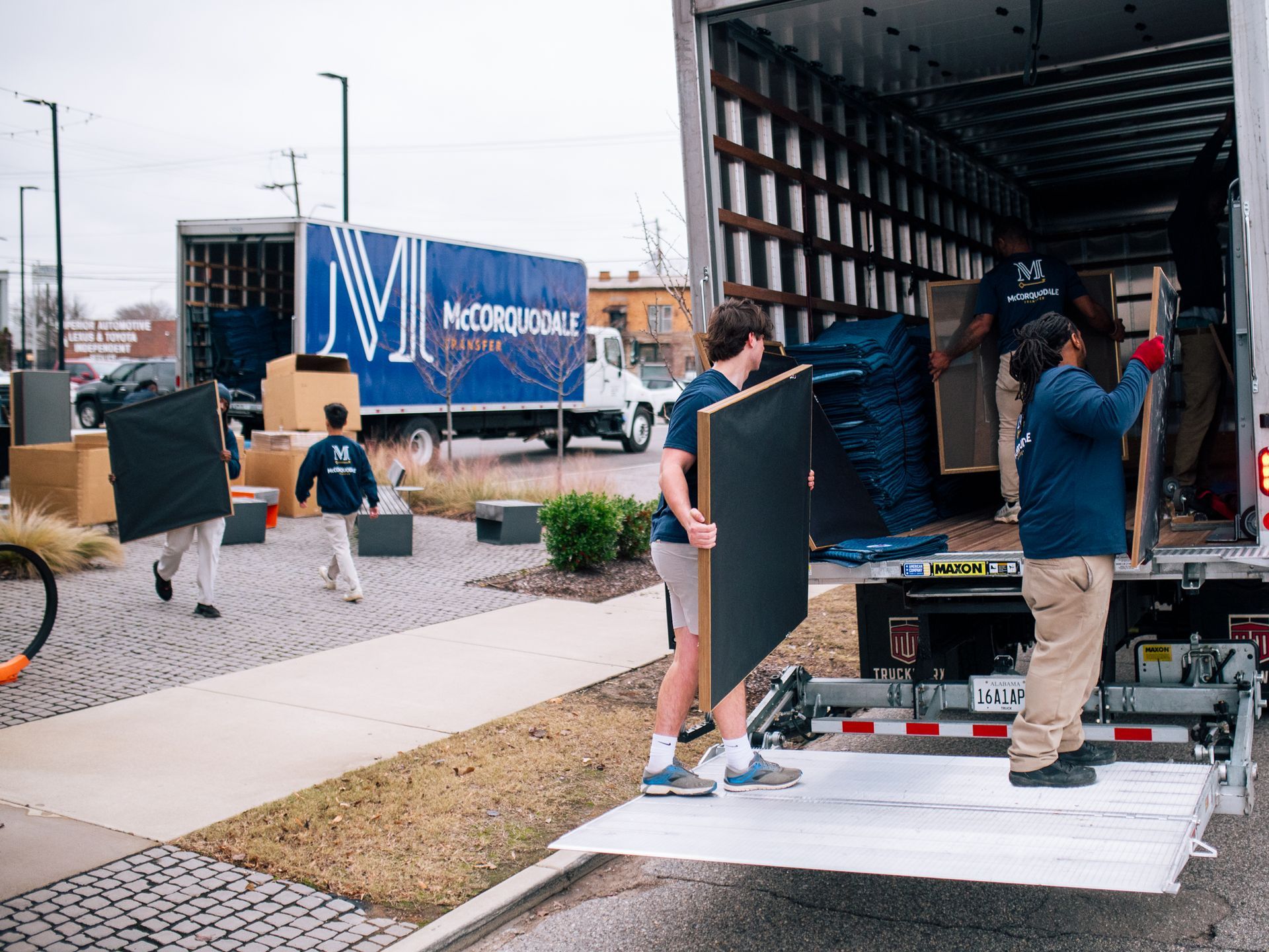 Movers loading a moving truck on a sidewalk in front of a building; daytime.