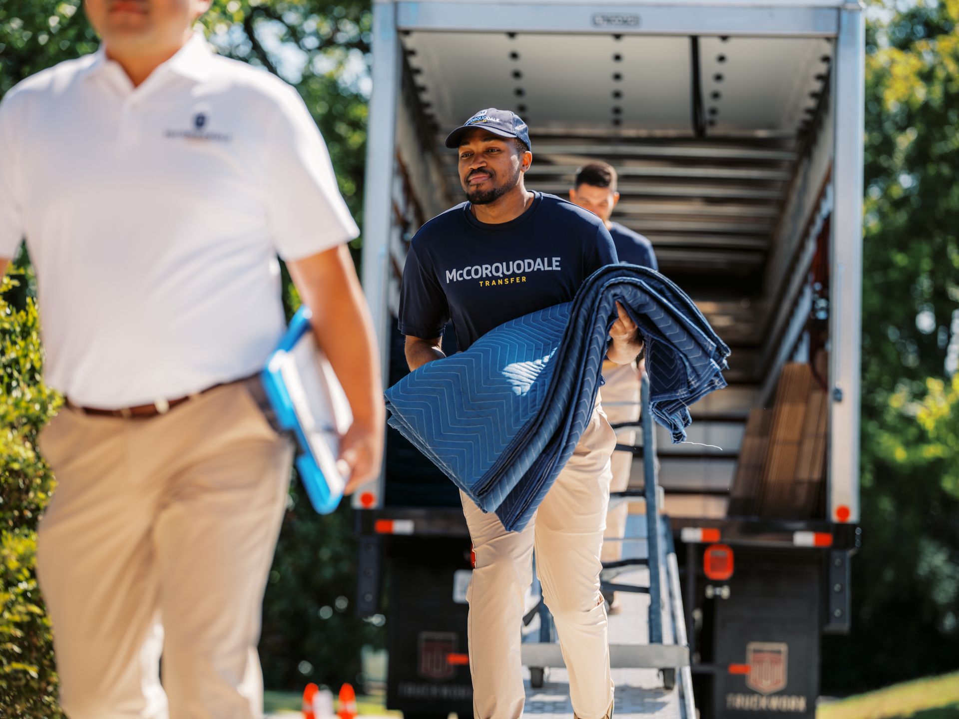 Man on a ladder smiling, loading a truck with assistance in an outdoor setting.
