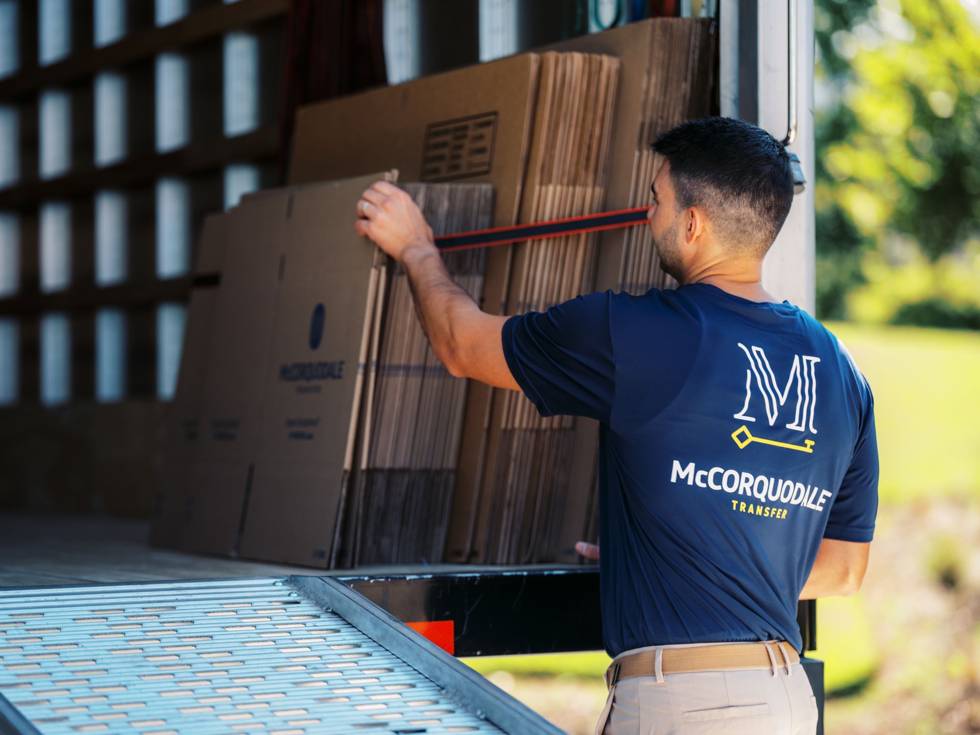 Man loading cardboard boxes into a truck, wearing a blue shirt with a logo on the back.
